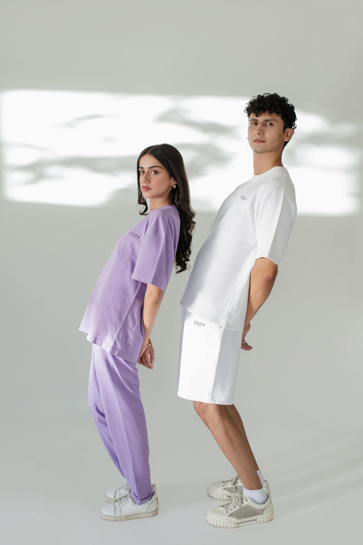 Models showcasing COZY Summer Collection in organic cotton t-shirts and shorts, featuring stylish purple and white outfits.