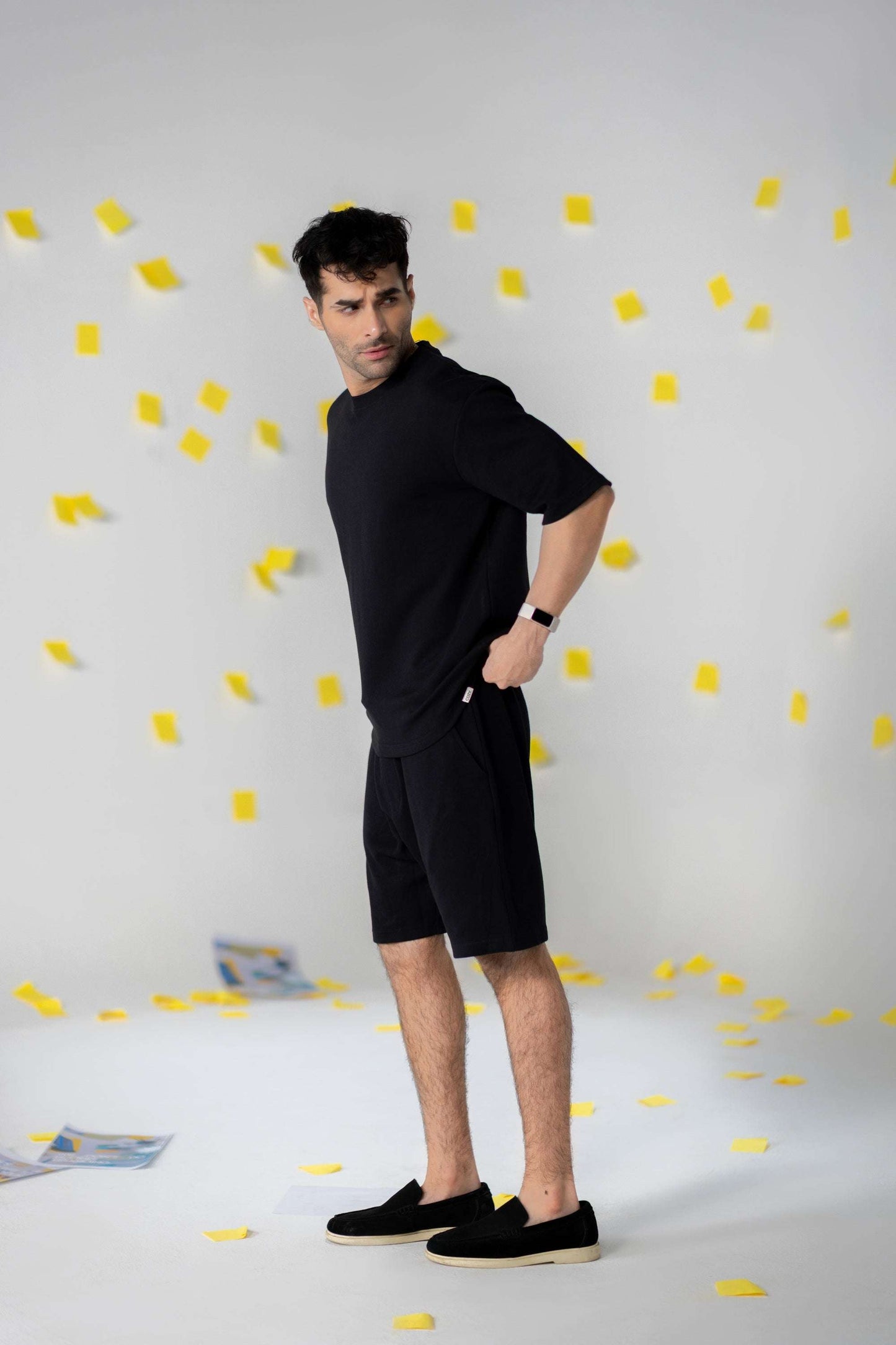 Man in black COZY Shorts V2, showcasing relaxed fit and organic cotton, set against a playful background of yellow notes.