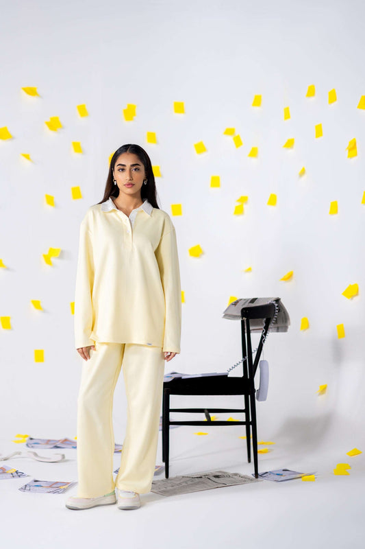 Model wearing COZY Ladies Rugby Polo in yellow, showcasing a relaxed fit, paired with matching pants, against a playful backdrop.