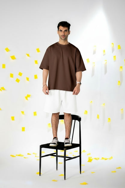 Model wearing COZY Shorts V2 and a brown oversized shirt, standing on a black chair surrounded by yellow paper.