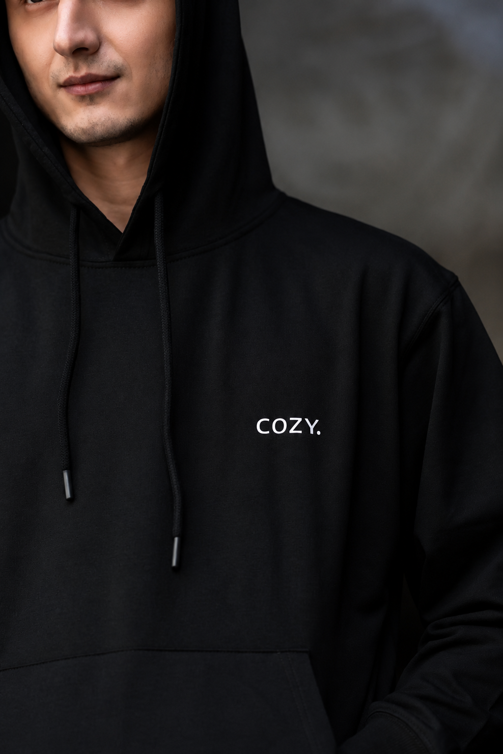 Close-up of the COZY Men's Hoodie in Dark Roast Black showing the small COZY logo on the chest, drawstrings and hood