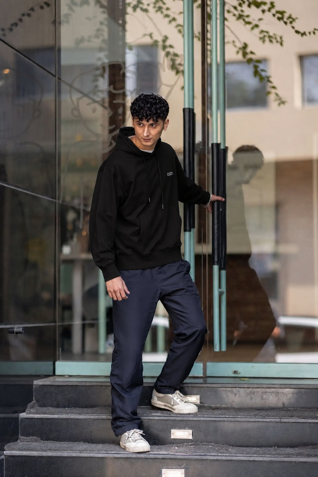 Side view of the COZY Men's Hoodie in Dark Roast Black, worn with dark trousers while stepping out of a glass door