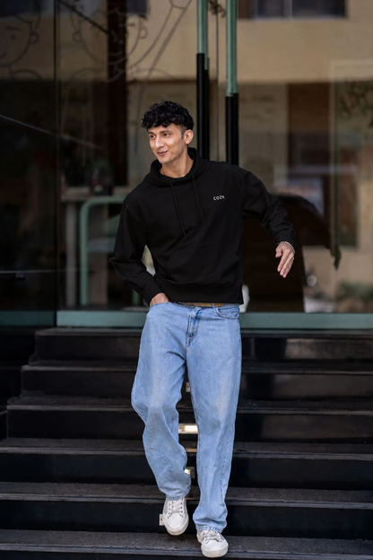 Man walking down dark steps in the COZY Men's Hoodie in Dark Roast Black with light wash jeans and white sneakers