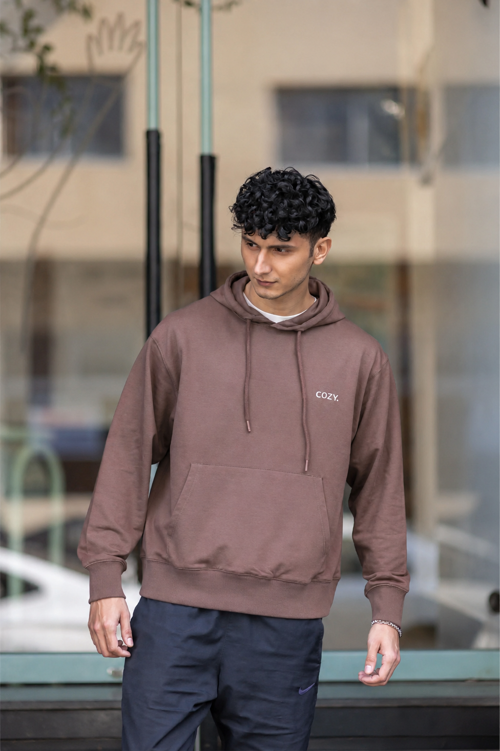 Front view of the COZY Men's Hoodie in Mocha Mousse, worn with dark trousers outside a glass storefront