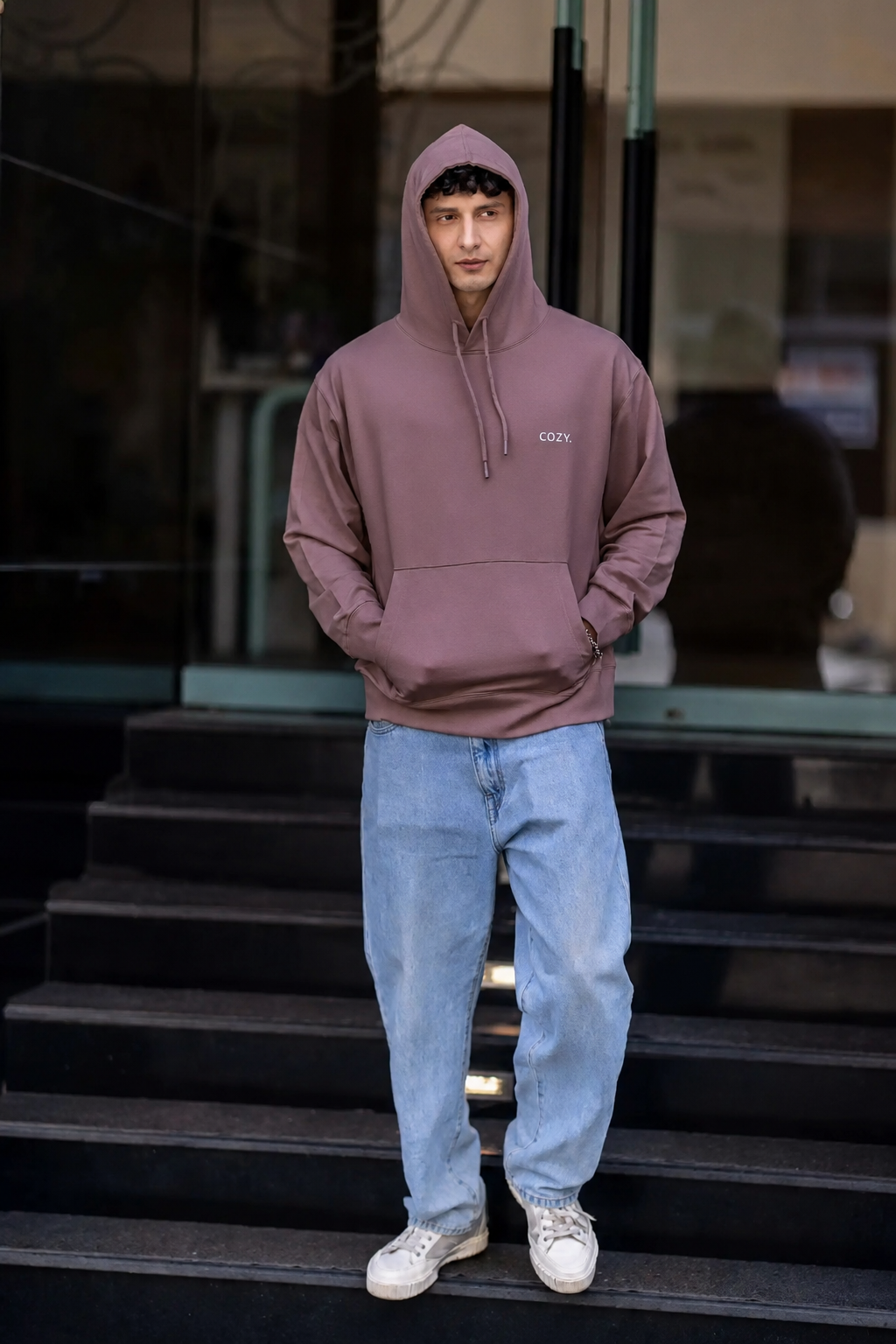 COZY Men's Hoodie in Mocha Mousse worn hood up with hands in the kangaroo pocket, full length on dark steps