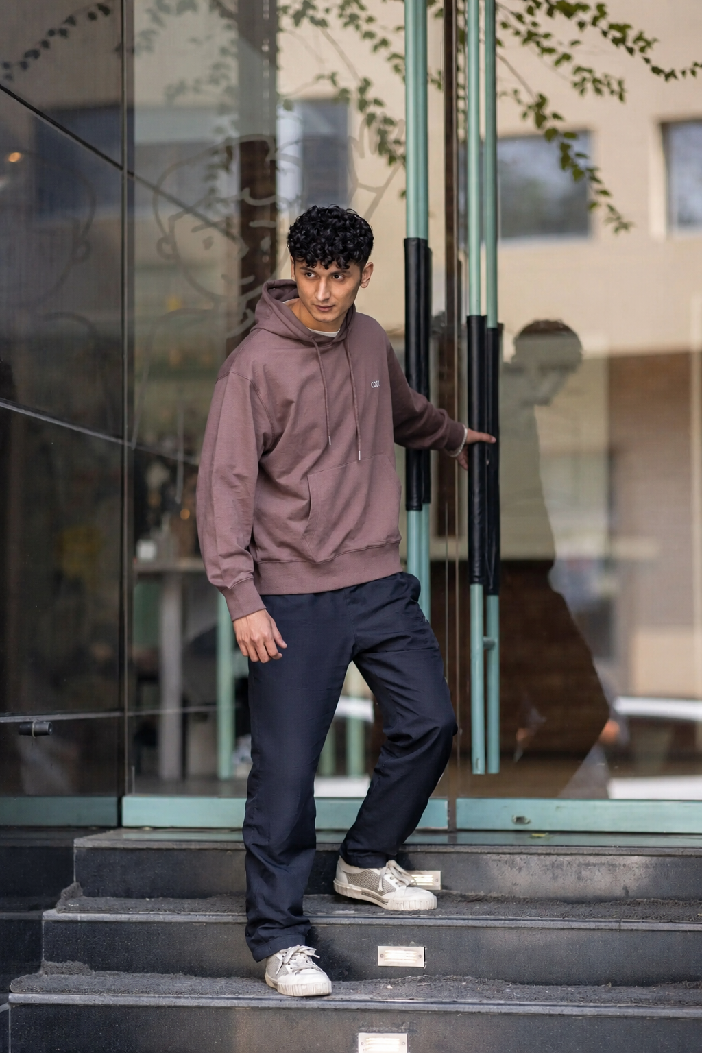 Side view of the COZY Men's Hoodie in Mocha Mousse, worn with dark trousers while stepping out of a glass door