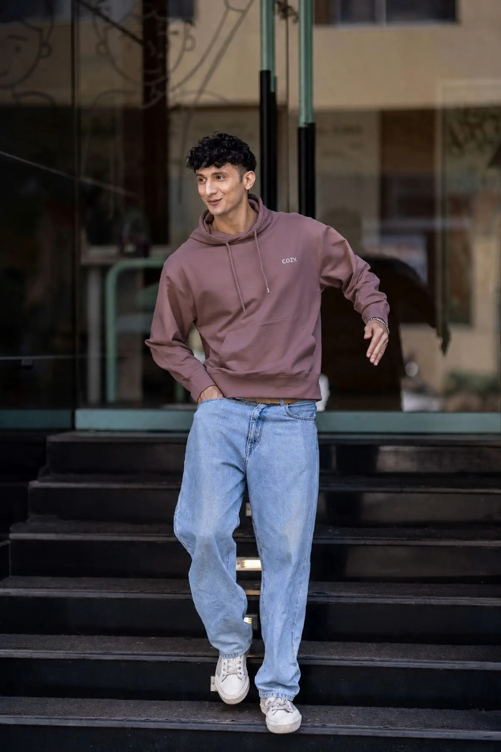 Man walking down dark steps in the COZY Men's Hoodie in Mocha Mousse with light wash jeans and white sneakers