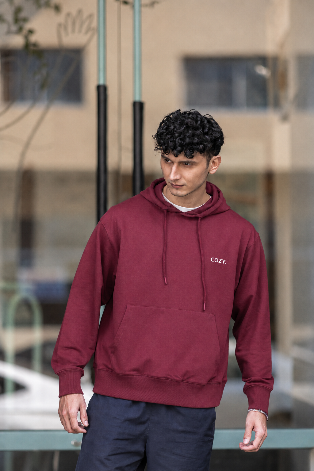Front view of the COZY Men's Hoodie in Mulberry Mocha, worn with dark trousers outside a glass storefront