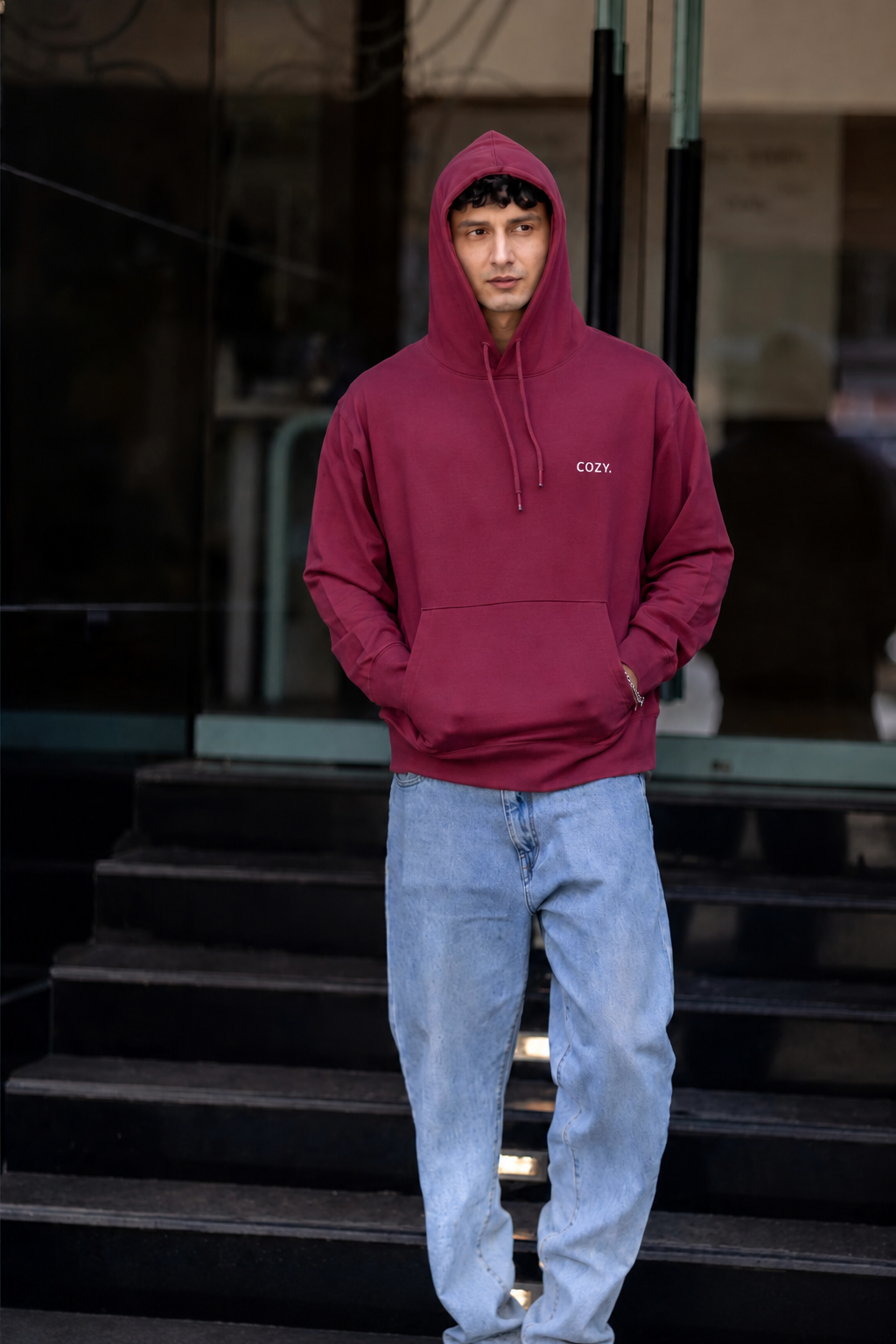 COZY Men's Hoodie in Mulberry Mocha worn hood up with hands in the pocket, light wash jeans, full length on steps