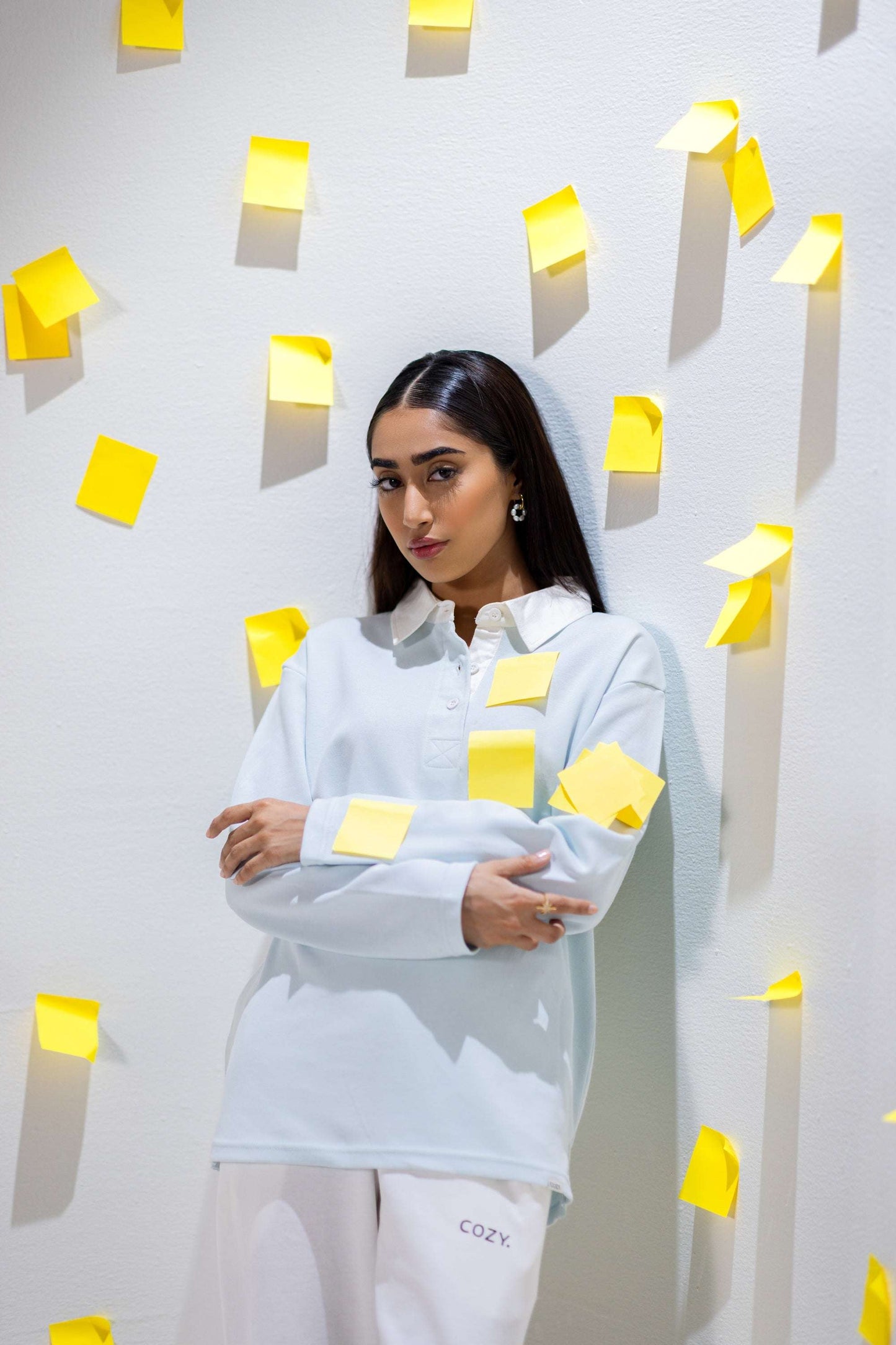 COZY Ladies Rugby Polo in light blue worn by a model surrounded by yellow sticky notes, showcasing relaxed fit and modern style.