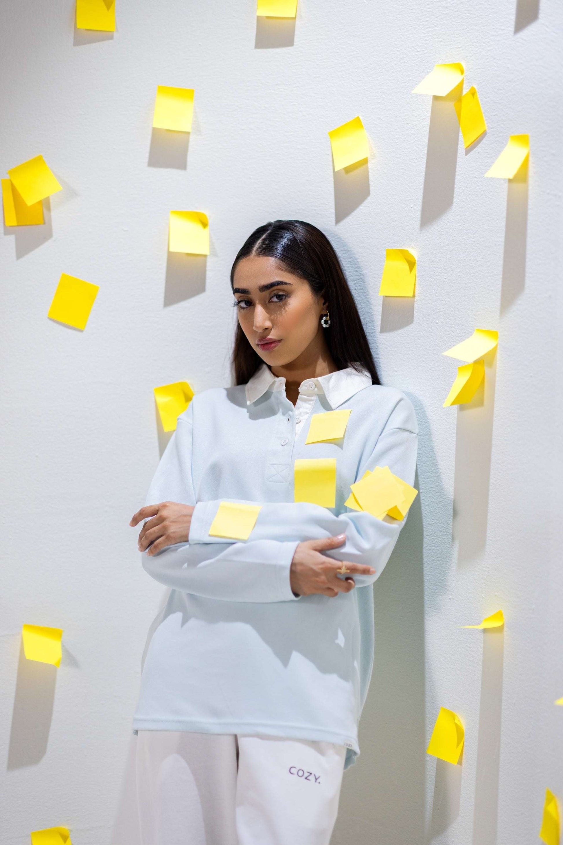 COZY Ladies Rugby Polo in light blue worn by a model surrounded by yellow sticky notes, showcasing relaxed fit and modern style.